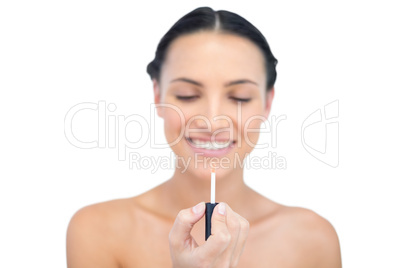 Cheerful young model holding and looking at her lip gloss