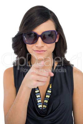 Elegant brunette wearing sunglasses pointing at camera