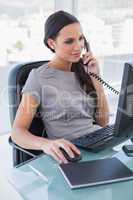 Concentrated businesswoman answering phone and working on comput