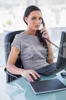 Serious businesswoman answering phone and working on computer