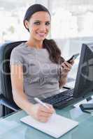 Cheerful businesswoman using calculator and writing