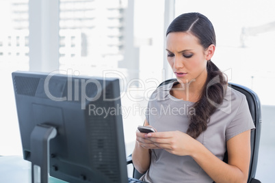 Frowning dark haired businesswoman sending message
