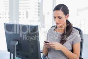 Frowning dark haired businesswoman sending message