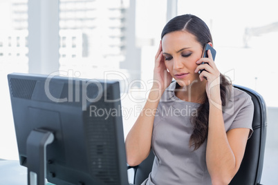 Dark haired businesswoman with headache having a phone conversat