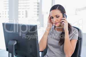Dark haired businesswoman with headache having a phone conversat