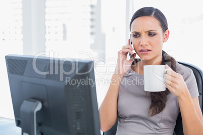 Frowning businesswoman holding coffee and answering phone