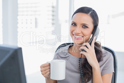Cheerful secretary answering phone and drinking coffee