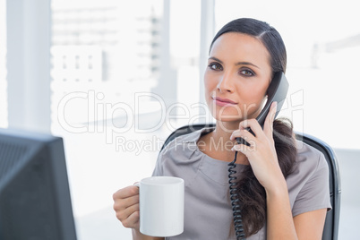 Serious secretary answering phone and drinking coffee
