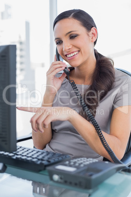 Smiling secretary answering land line and pointing at computer s