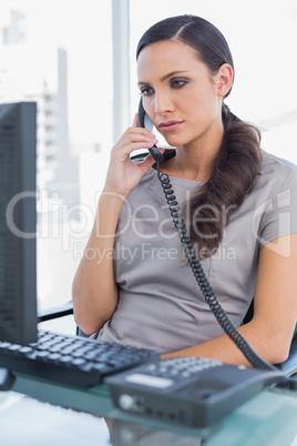 Serious secretary answering land line looking at computer screen
