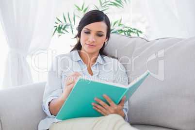 Concentrated gorgeous brunette writing while sitting on the sofa