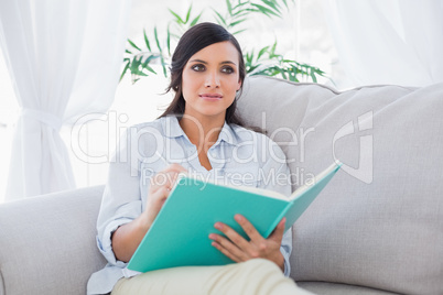 Pensive gorgeous brunette writing while sitting on the sofa