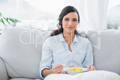 Pretty woman sitting on the couch eating fruit salad