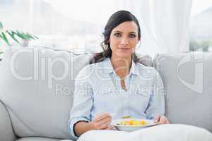 Pretty woman sitting on the couch eating fruit salad
