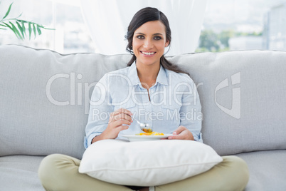 Woman sitting on the couch crossing legs eating fruits