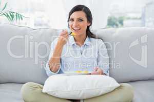 Cheerful woman sitting on the couch crossing legs eating fruits