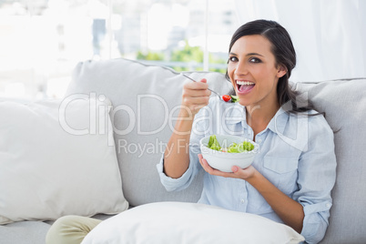 Cheerful woman relaxing on the sofa eating salad