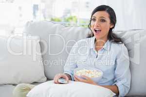 Astonished woman relaxing on the sofa eating popcorn