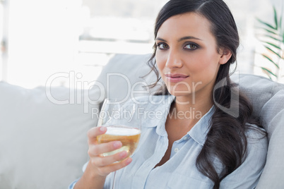 Pretty brunette drinking white wine sitting on sofa