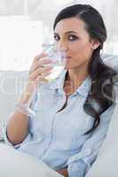 Attractive brunette drinking white wine sitting on sofa