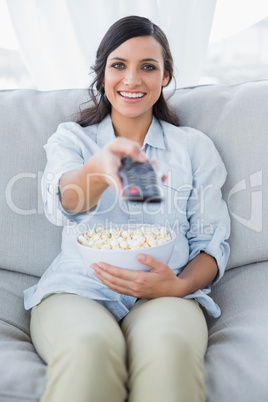 Cheerful pretty brunette watching tv and eating pop corn