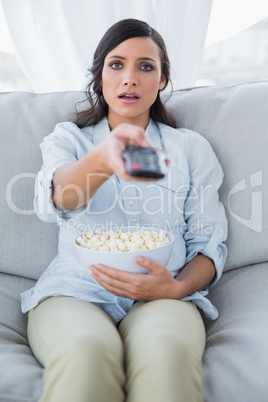 Surprised pretty brunette watching tv and eating pop corn
