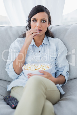 Concentrated pretty brunette watching tv and eating pop corn