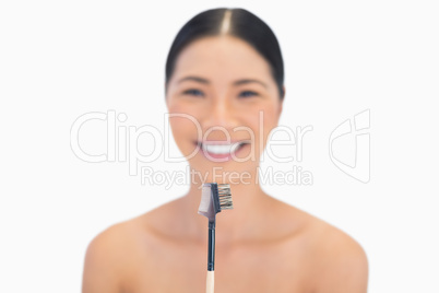 Smiling natural model holding eyebrow brush in front of her