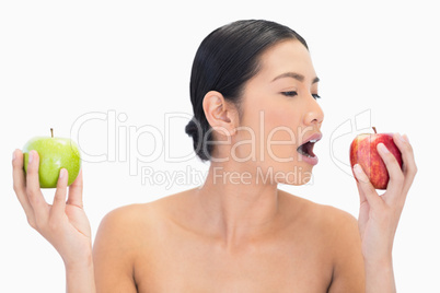 Black haired model holding apples in both hands eating the red o
