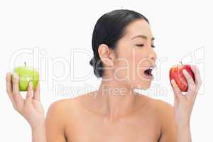 Black haired model holding apples in both hands eating the red o