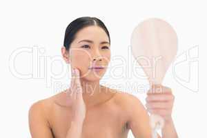 Natural dark haired model holding mirror touching her cheek