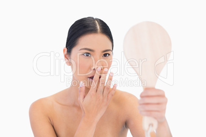Natural dark haired model holding mirror touching her nose