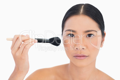 Serious dark haired woman applying powder on her face