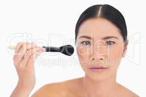 Serious dark haired woman applying powder on her face