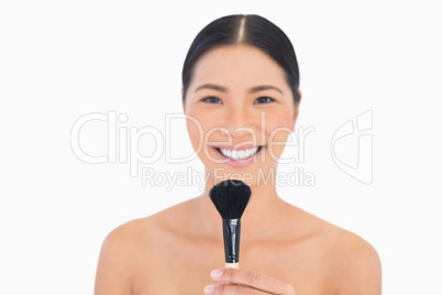 Smiling dark haired woman holding powder brush in front of her