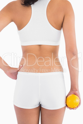 Back of female slender body in shorts holding orange in right ha