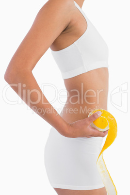 Profile of female slender body in sport underwear holding orange
