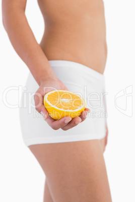 Slender female body holding half orange