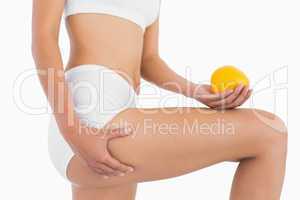Female body holding orange and squeezing her thigh