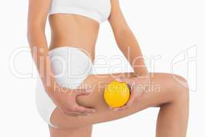 Slender female body holding orange and squeezing her thigh