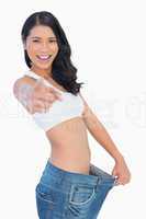 Victorious woman holding her too big pants and pointing out at c