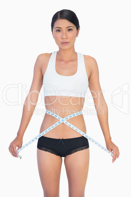 Serious slim woman measuring her waist