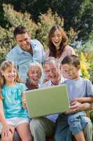 Happy multi generation family with a laptop sitting in park