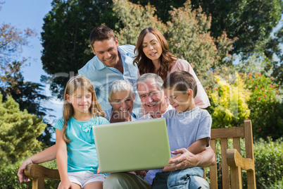 Smiling multi generation family with a laptop sitting in park