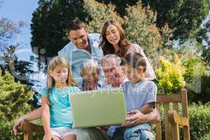 Smiling multi generation family with a laptop sitting in park