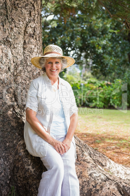 Smiling retired woman sitting on tree trunk