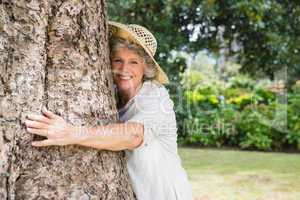 Retired woman hugging a tree smiling at camera