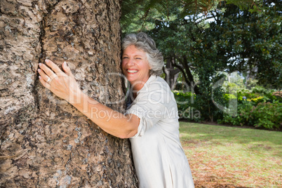 Smiling older woman hugging a tree