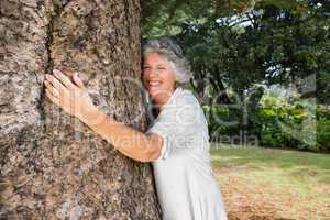 Smiling older woman hugging a tree
