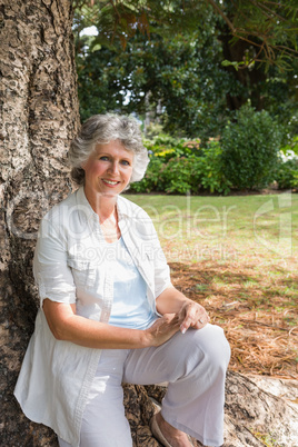 Happy mature woman sitting on tree trunk